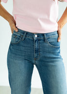 Person wearing blue jeans and a pink top with a plain background