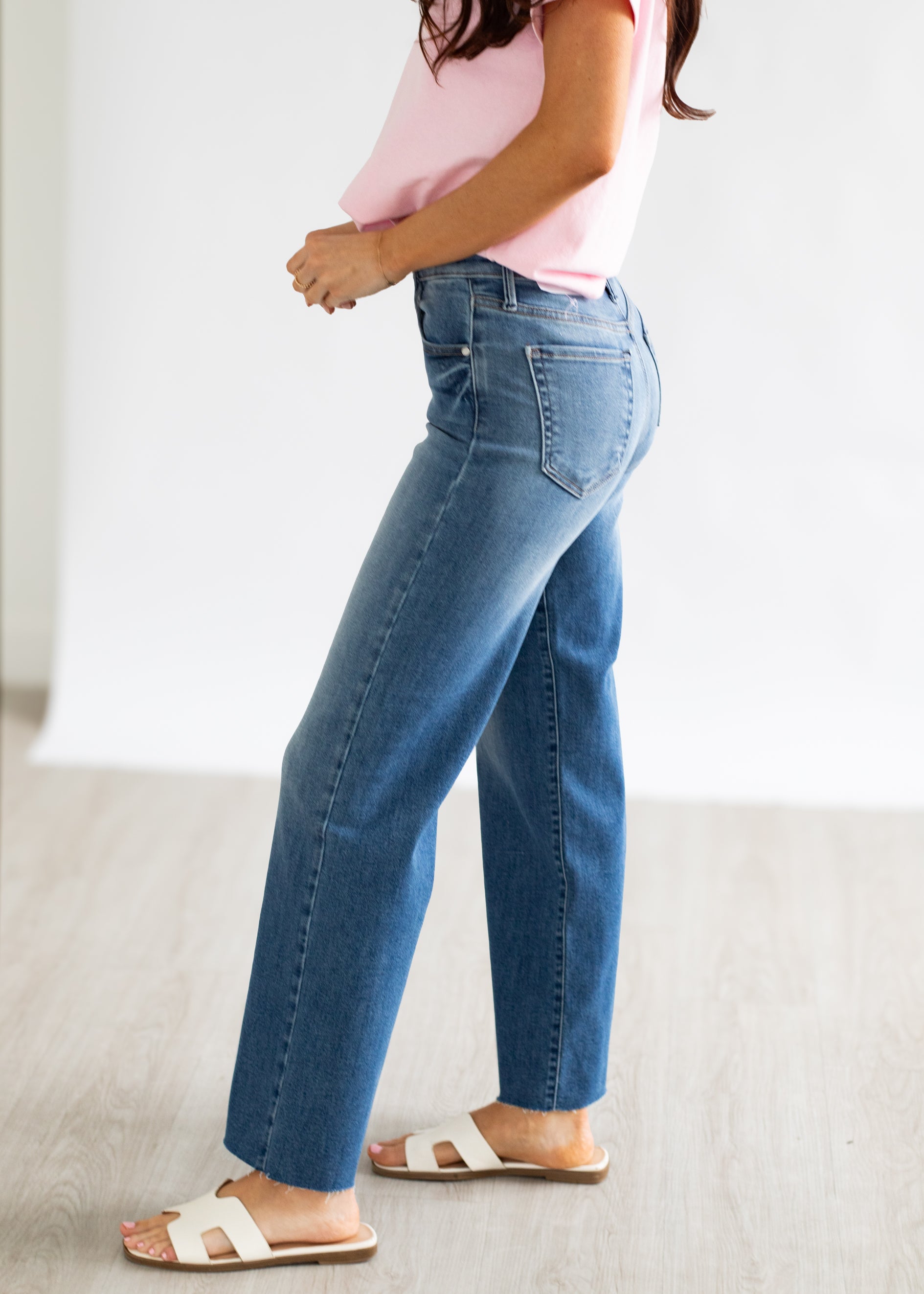 Person wearing blue jeans and a pink top on a plain background
