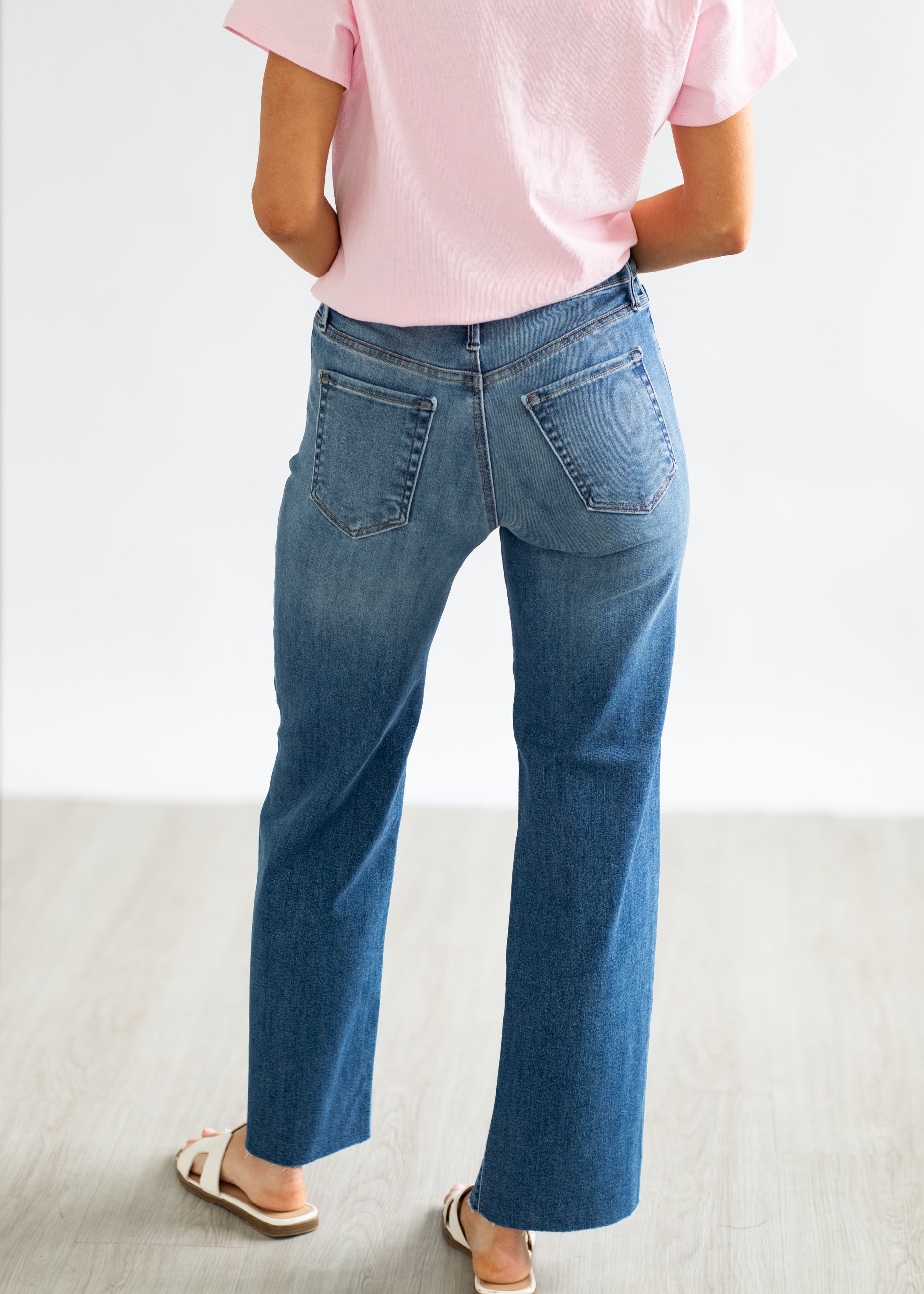 Person wearing blue jeans and a pink shirt on a light background