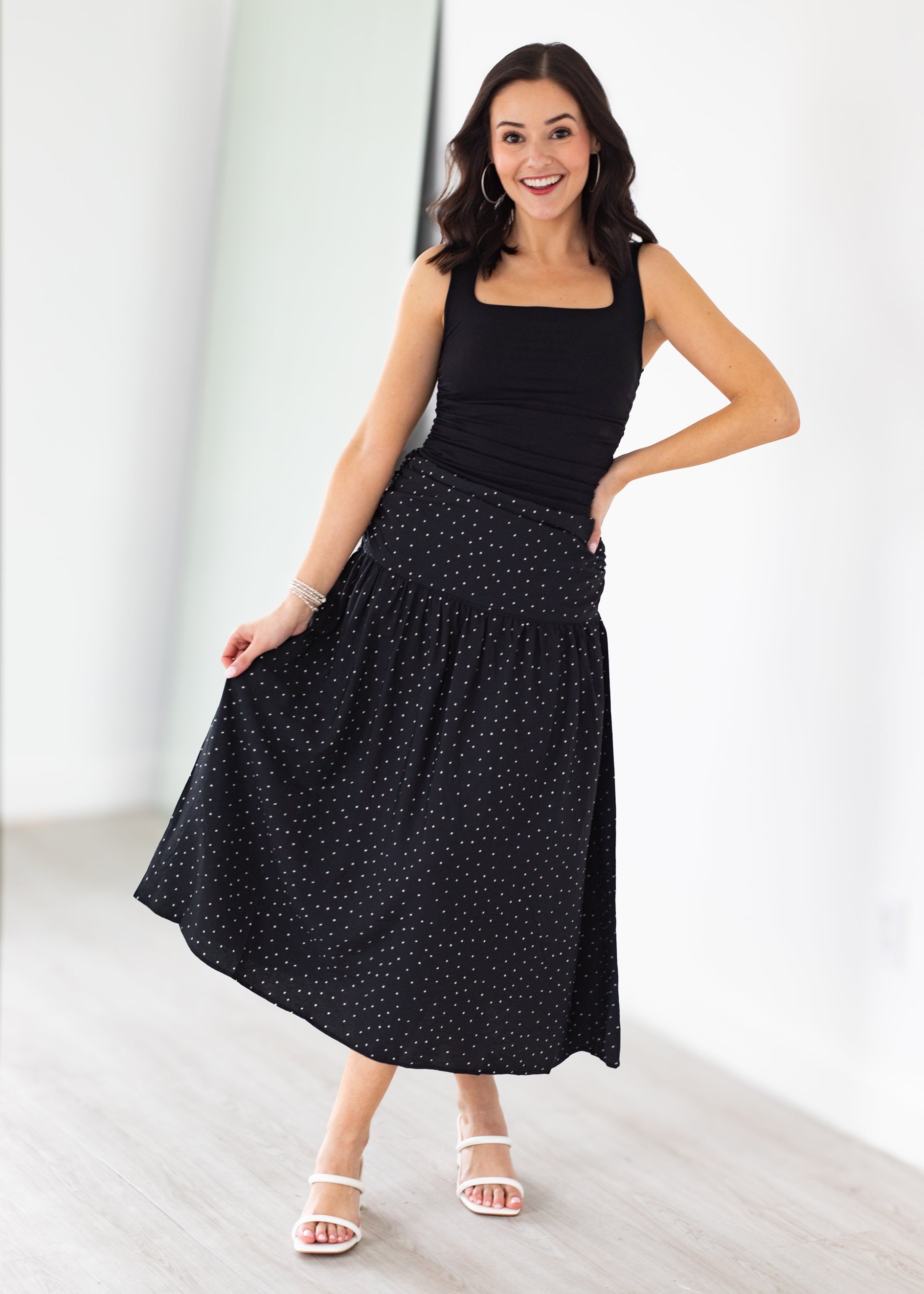 Woman wearing a black sleeveless top and black polka dot skirt on a white background