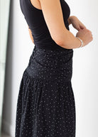 Person wearing a black sleeveless top and black polka dot skirt on a white background