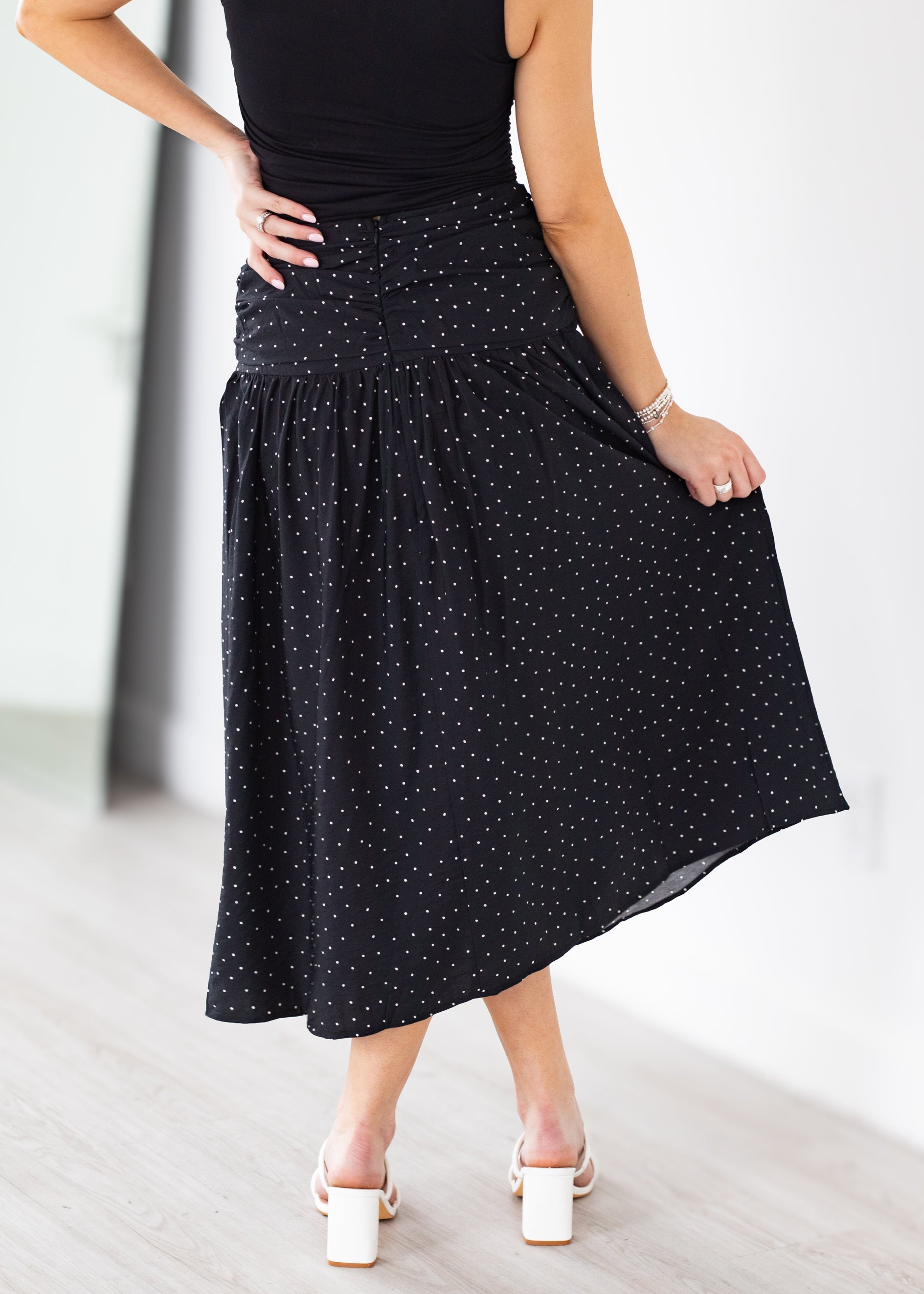 Person wearing a black polka dot skirt on a light background