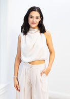 Woman wearing a white sleeveless top and pants against a white background
