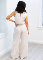 Woman wearing a beige jumpsuit in a minimal white room