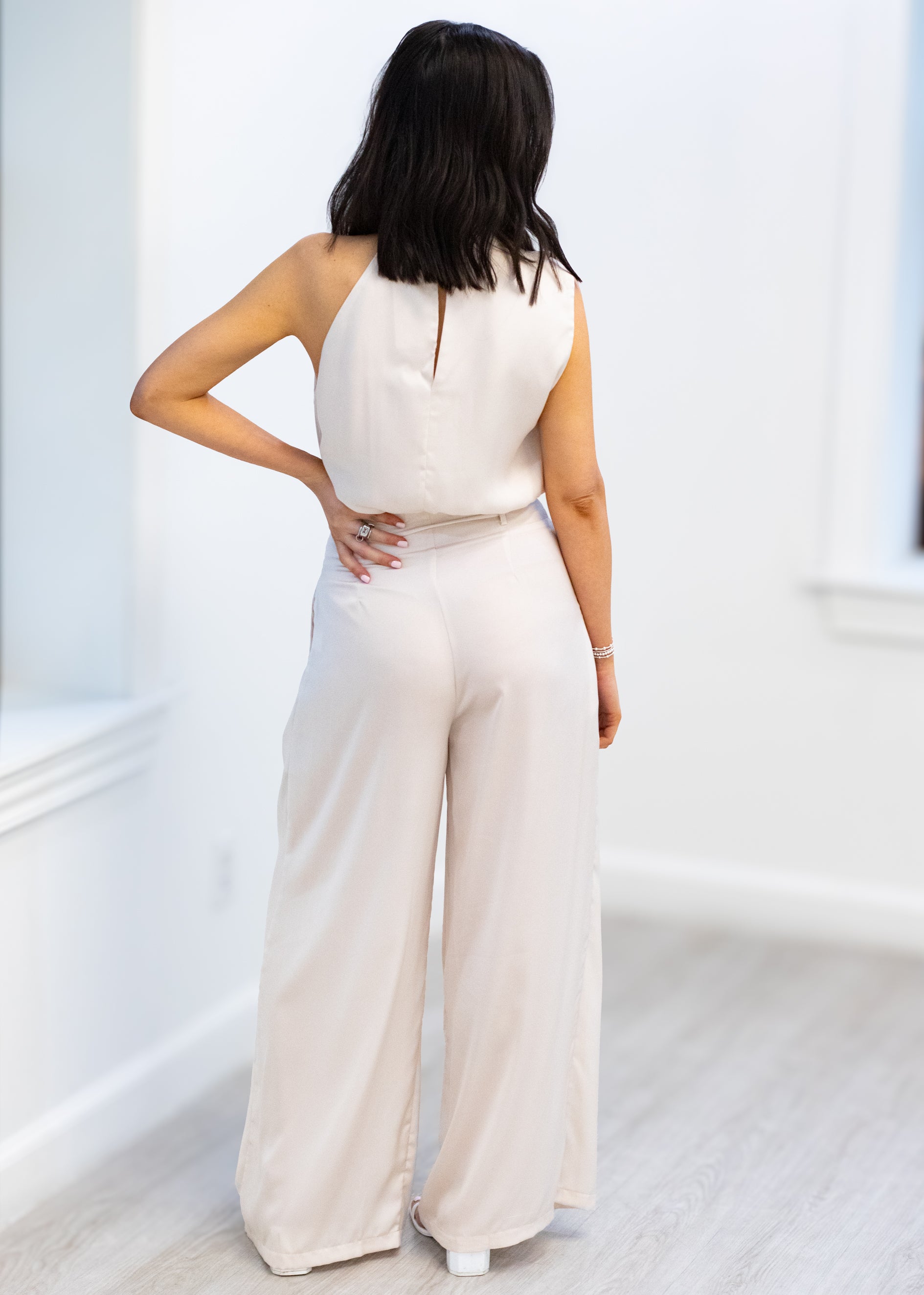 Woman wearing a beige jumpsuit in a minimal white room
