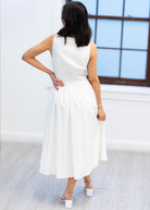 Woman wearing a white dress standing in a minimalistic room with a large window.