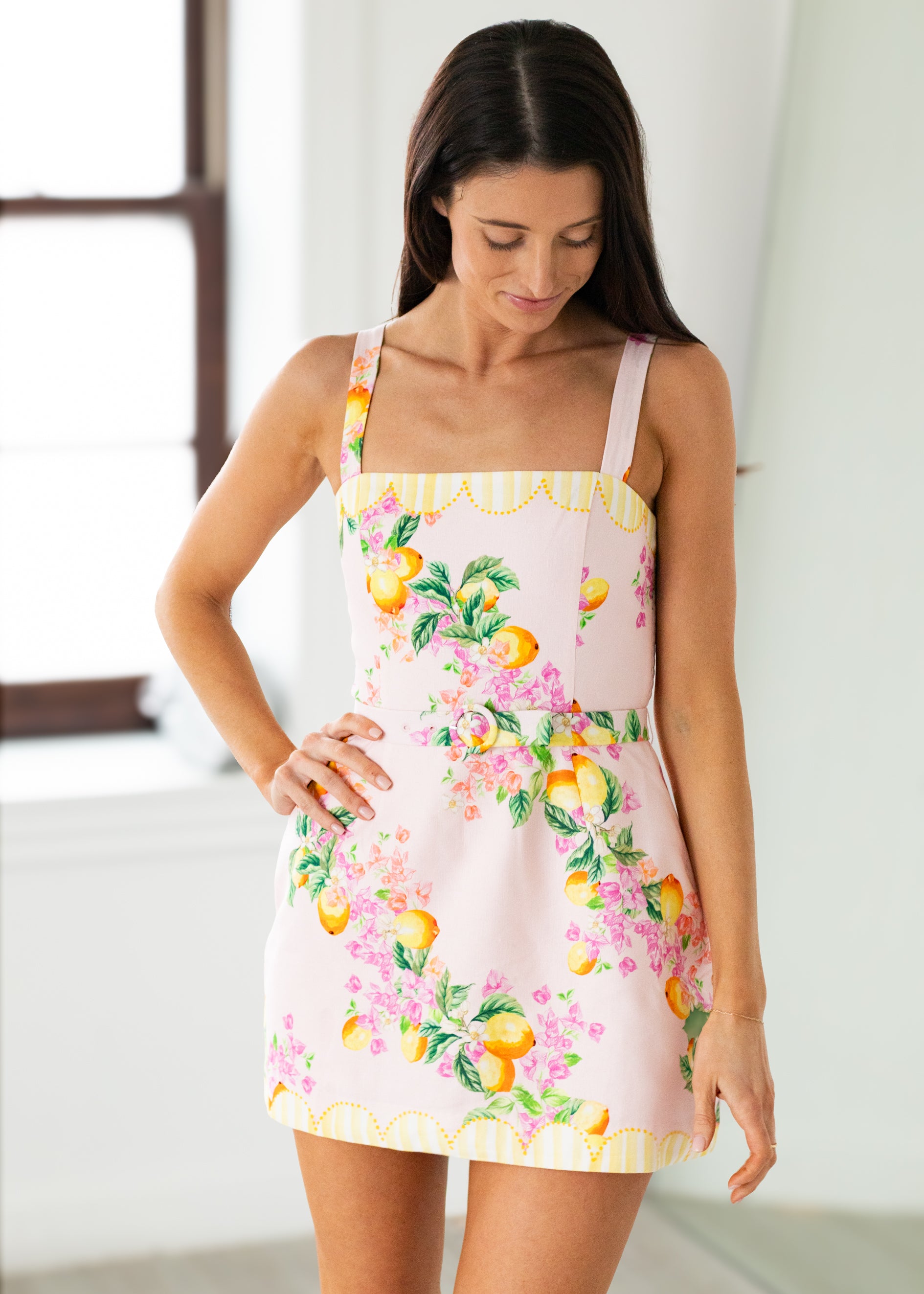 Woman wearing a floral apron with fruit design in a bright room.