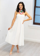 Woman wearing a white dress with a colorful scarf in a minimal indoor setting