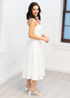 Woman in a white dress standing in a minimalistic room with a window.