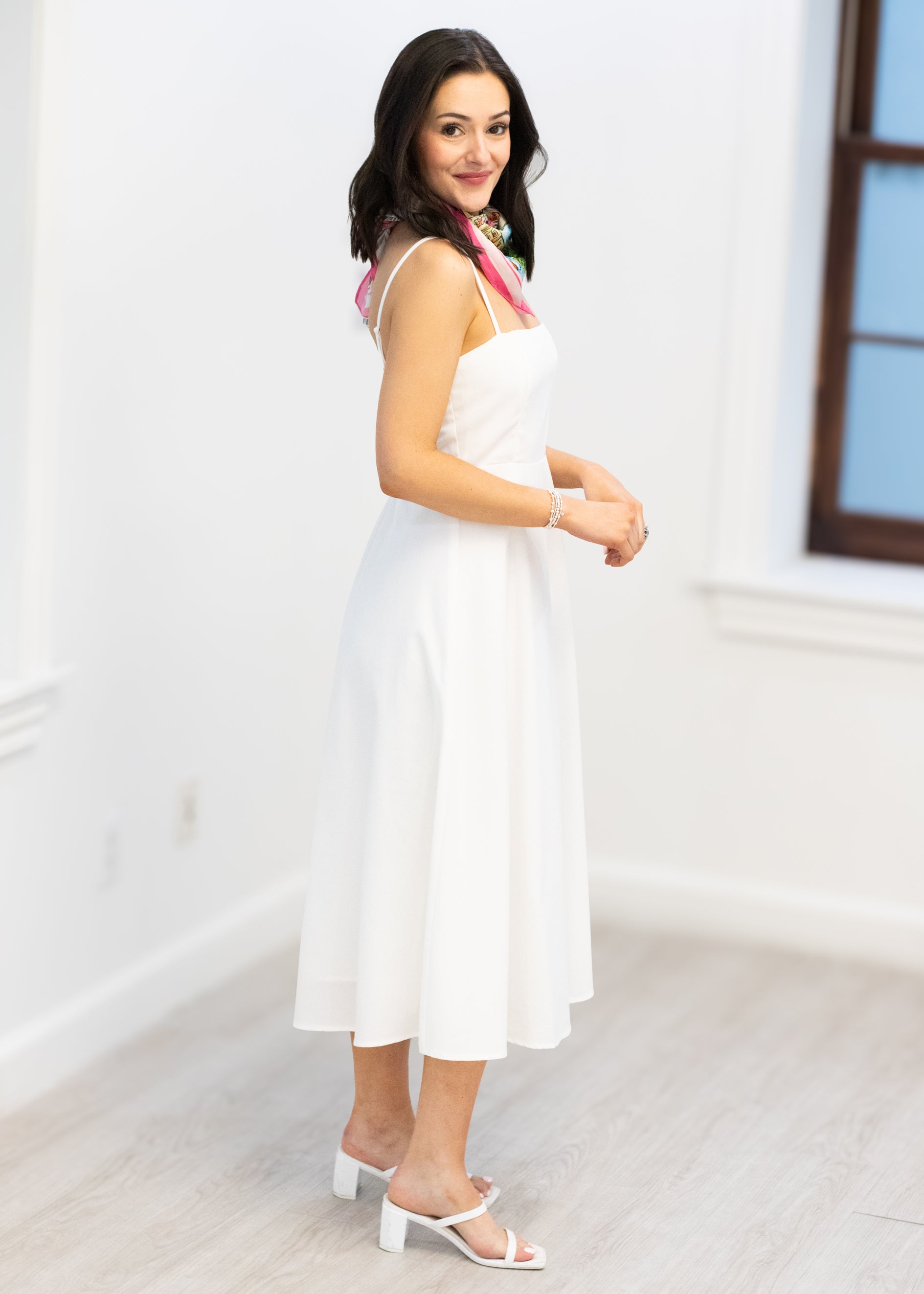 Woman in a white dress standing in a minimalistic room with a window.