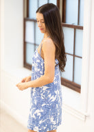 Woman wearing a blue floral dress standing in front of a window.