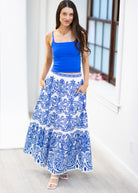 Woman wearing a blue top and white skirt with blue patterns indoors.