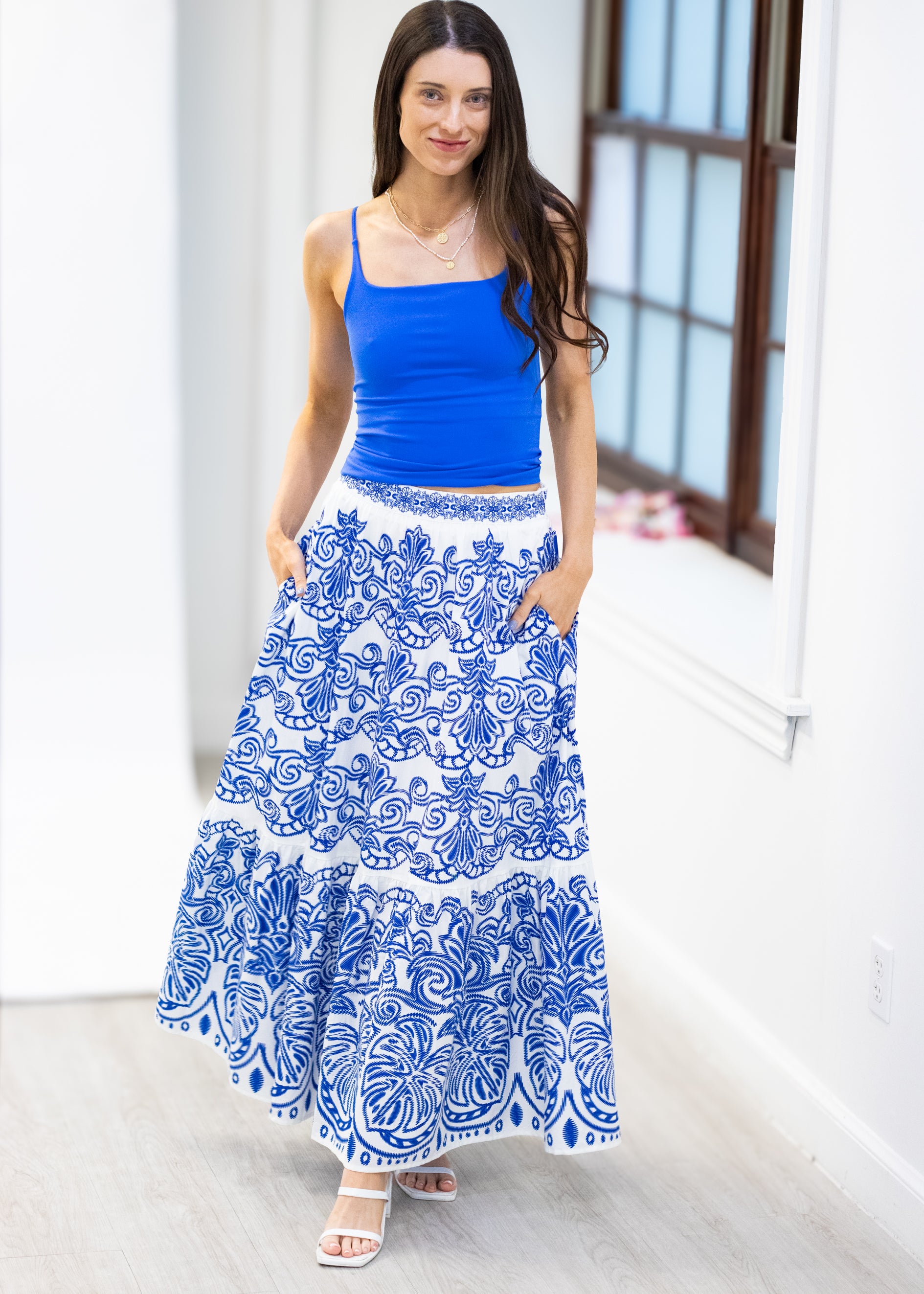 Woman wearing a blue top and white skirt with blue patterns indoors.