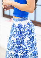 Person wearing a blue top and white patterned skirt with a blurred background