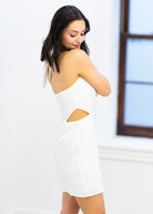 Woman wearing a white dress with cut-out design in a bright room.