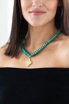 Woman wearing a green beaded necklace with a gold clover pendant against a white background