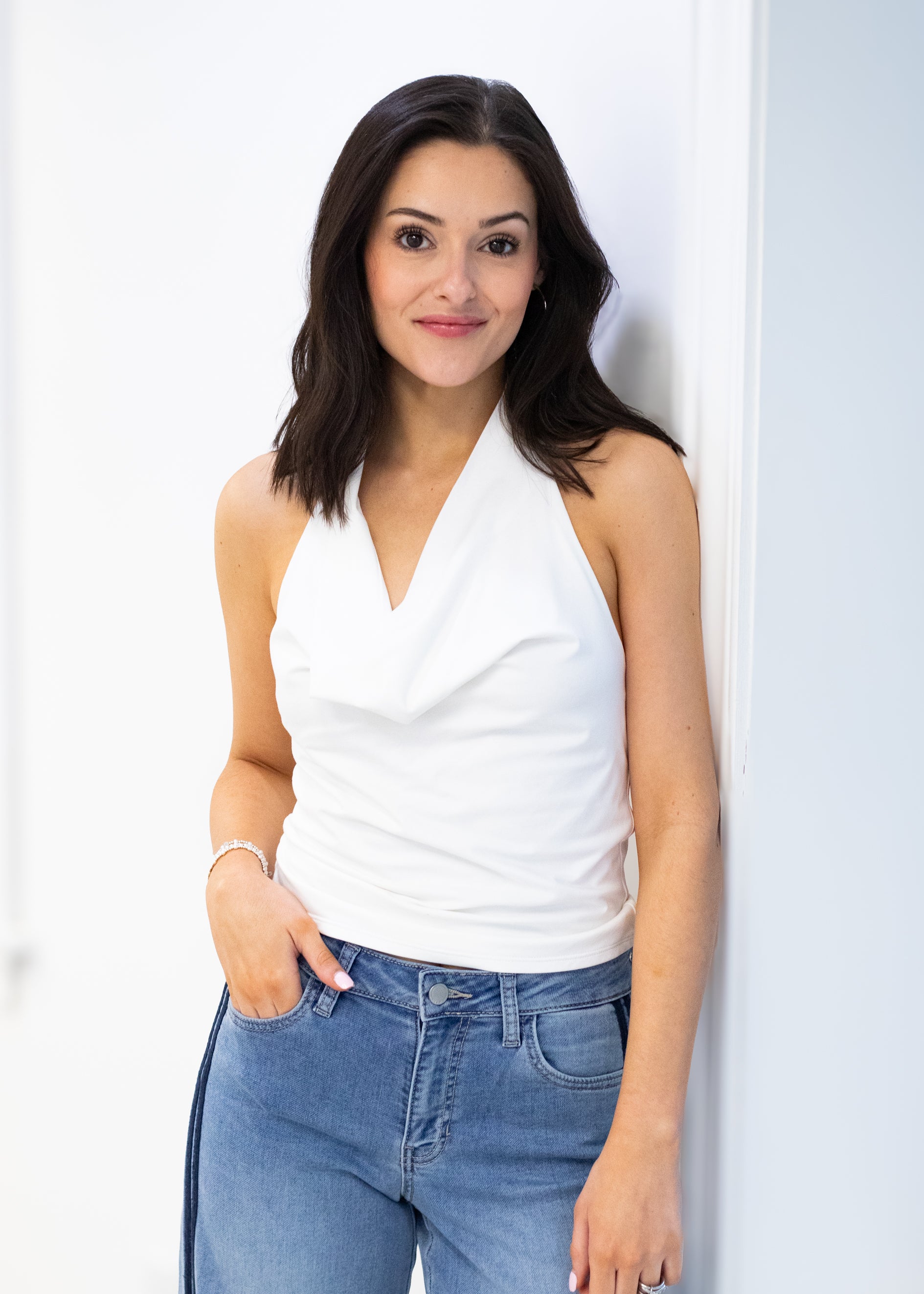 Woman wearing a white sleeveless top and blue jeans against a white background