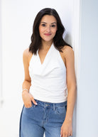 Woman wearing a white sleeveless top and blue jeans against a white background