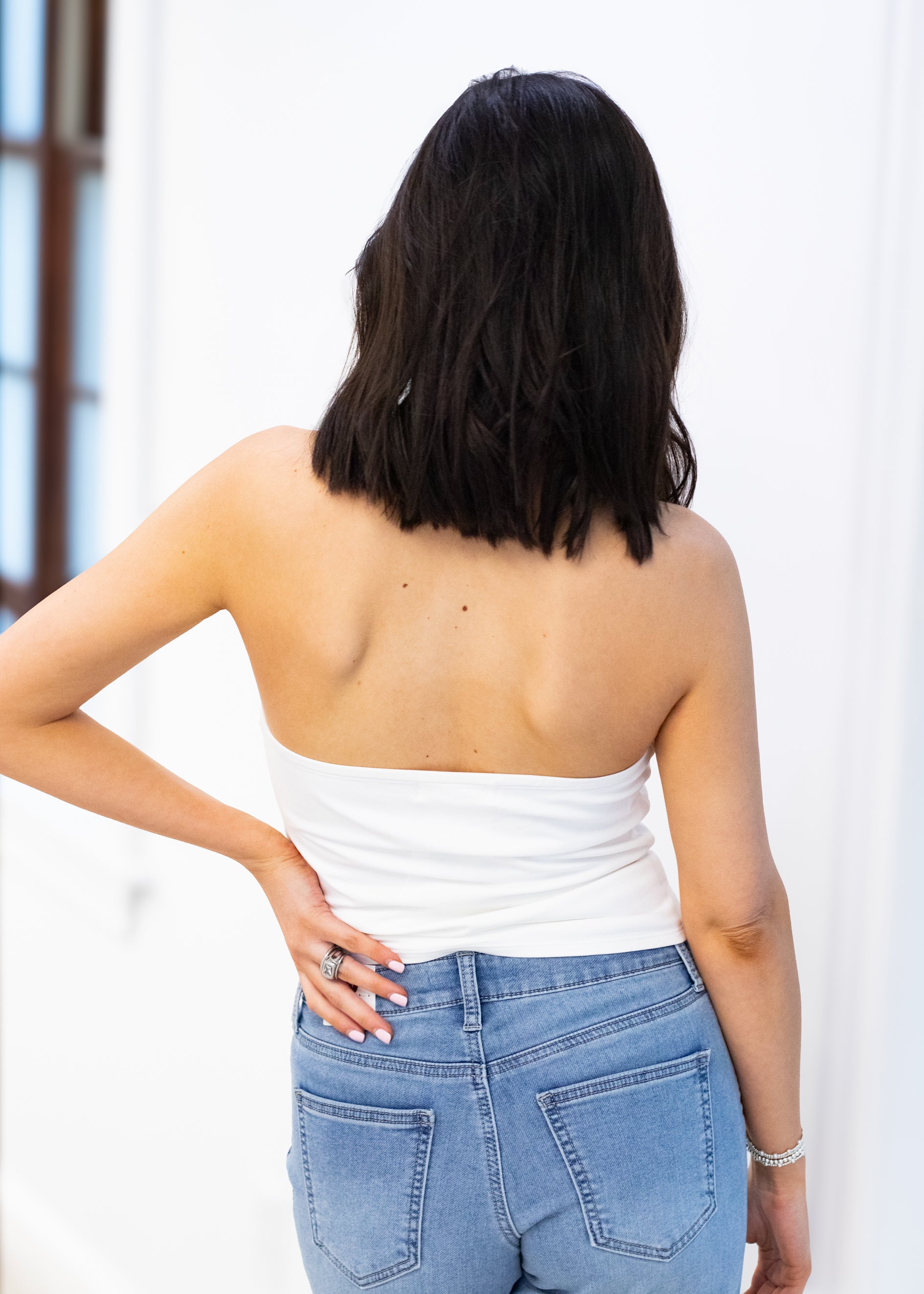 Person wearing a white strapless top and blue jeans with a blurred background