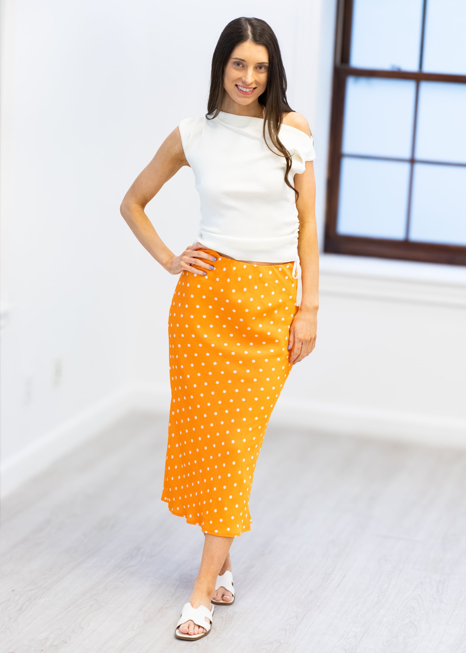 Woman wearing a white top and orange polka dot skirt on a plain background