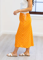 Person wearing an orange polka dot skirt with a white top on a light background