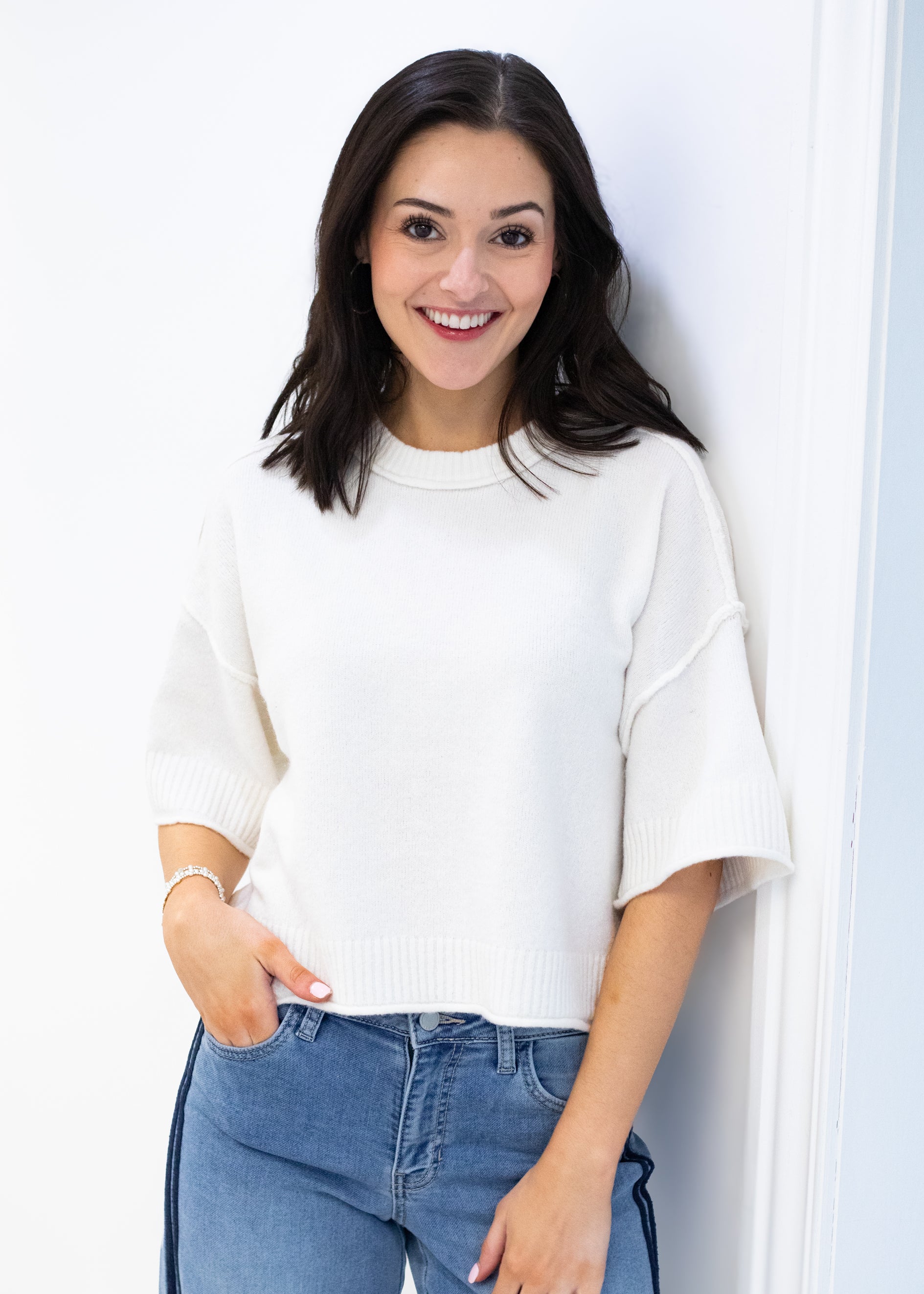 Woman wearing a white sweater and blue jeans against a white background