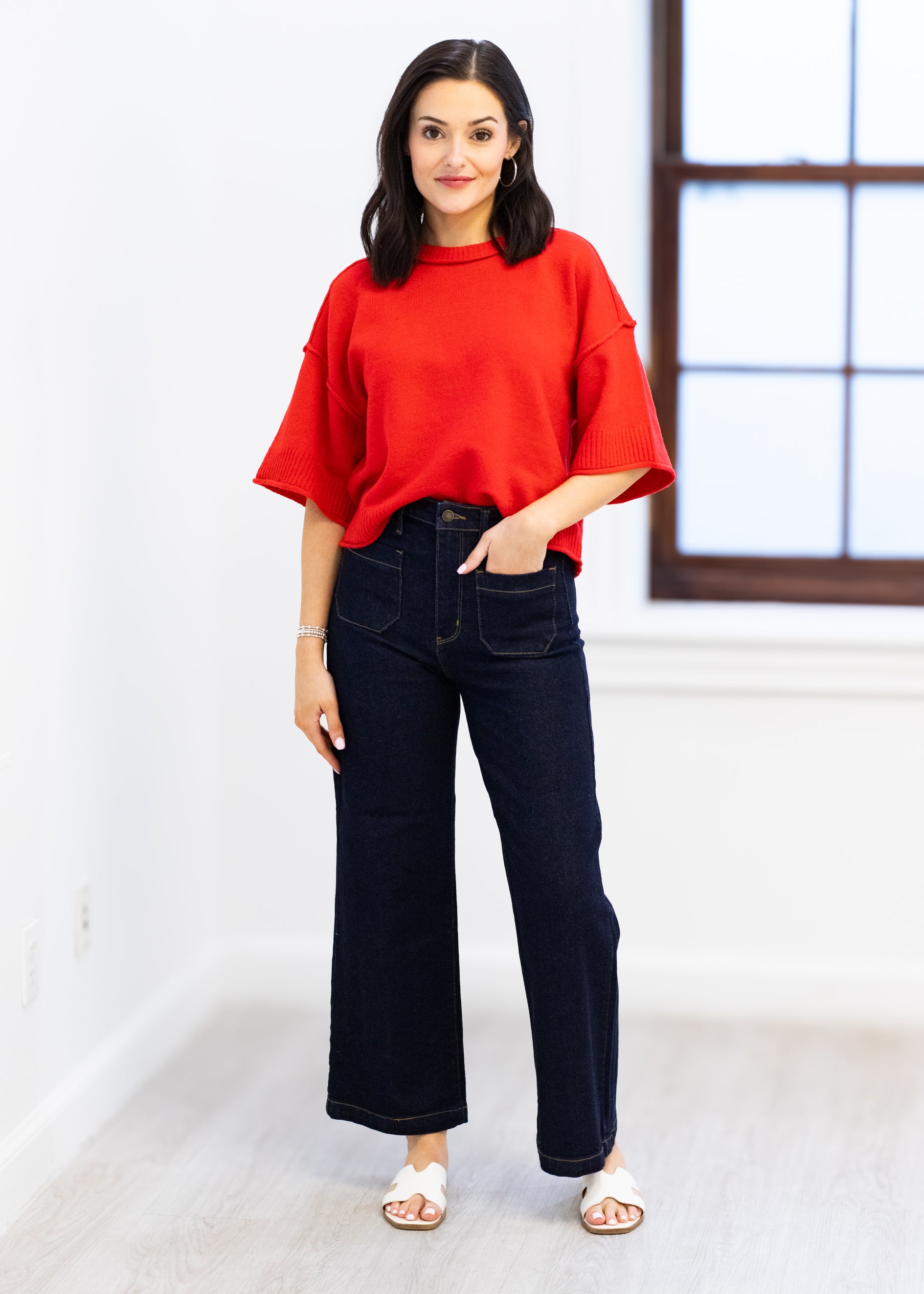 Woman wearing a red top and black jeans standing indoors.