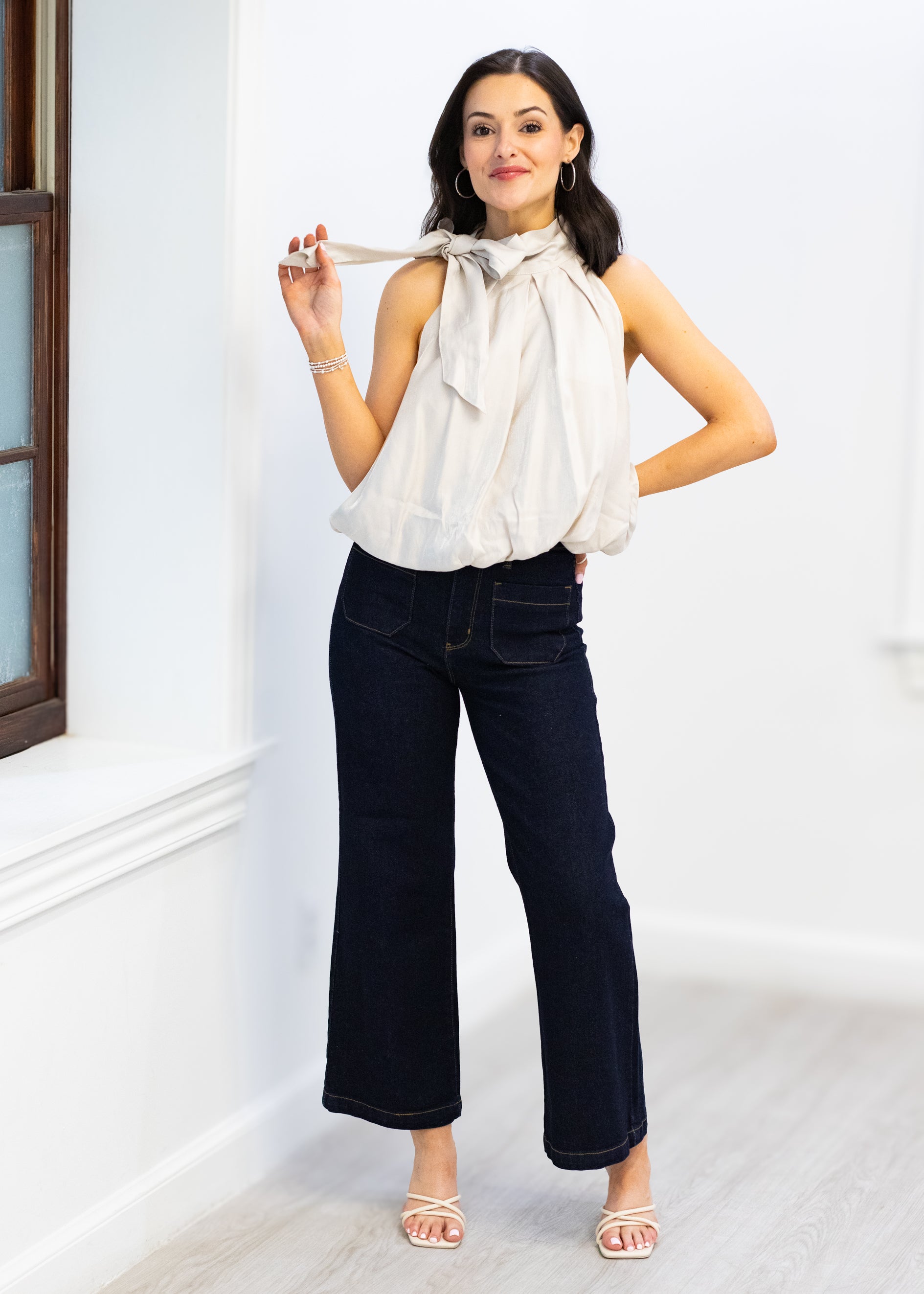 Woman wearing a white blouse with a bow and dark jeans indoors.