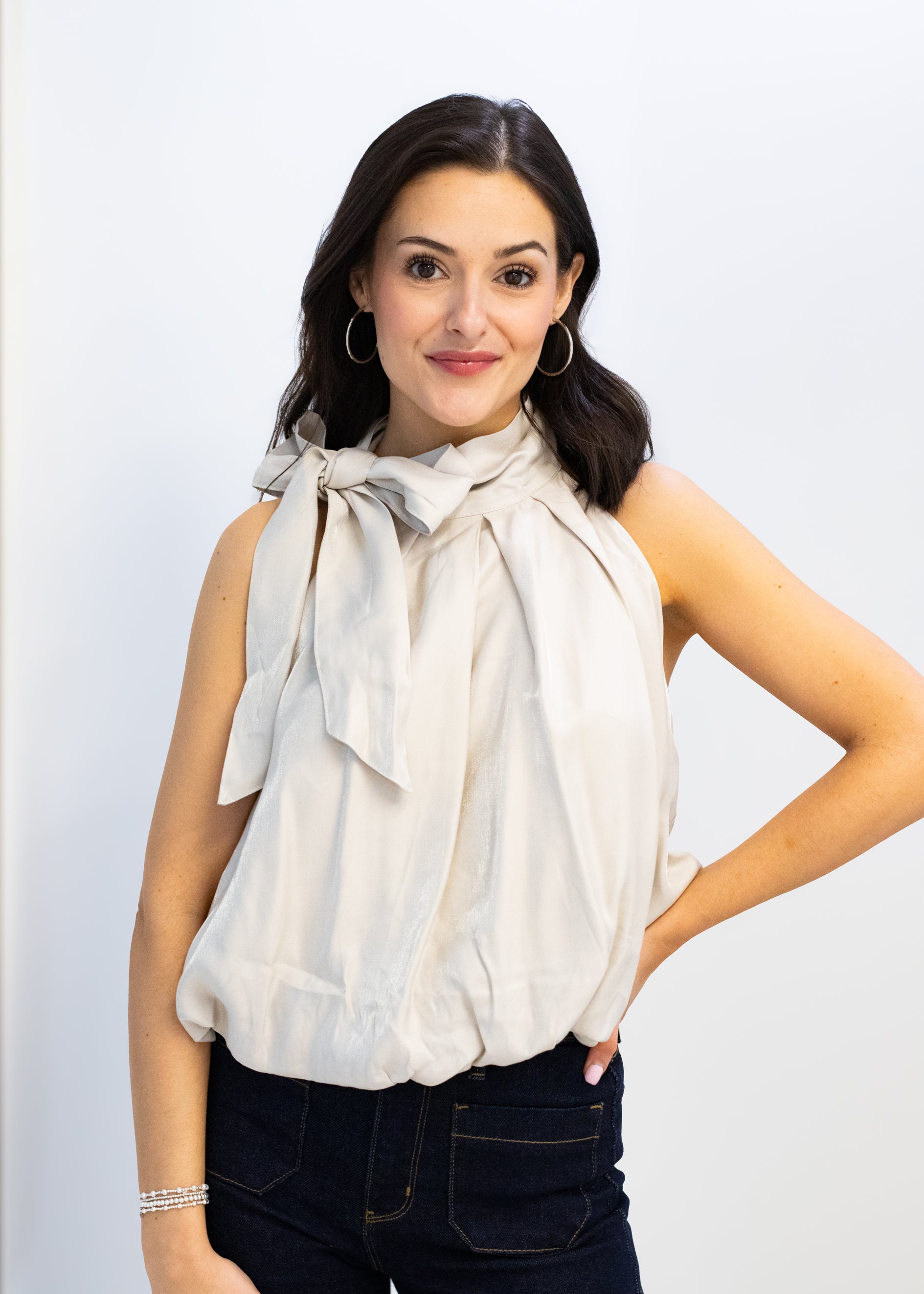 Woman wearing a beige blouse with a bow tie against a plain background