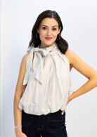 Woman wearing a beige blouse with a bow tie against a plain background