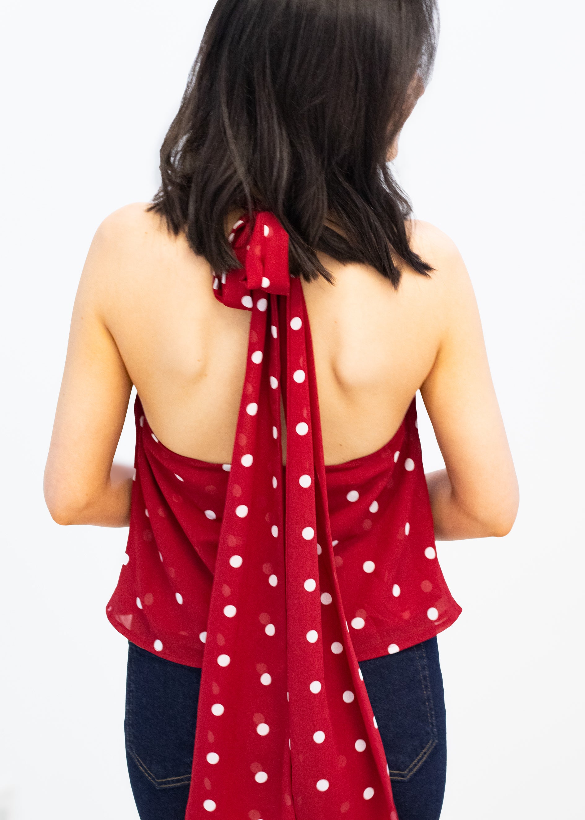 Red polka dot top worn by a person on a white background