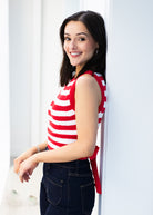 Woman wearing a red and white striped sleeveless top and dark jeans, standing against a white background.