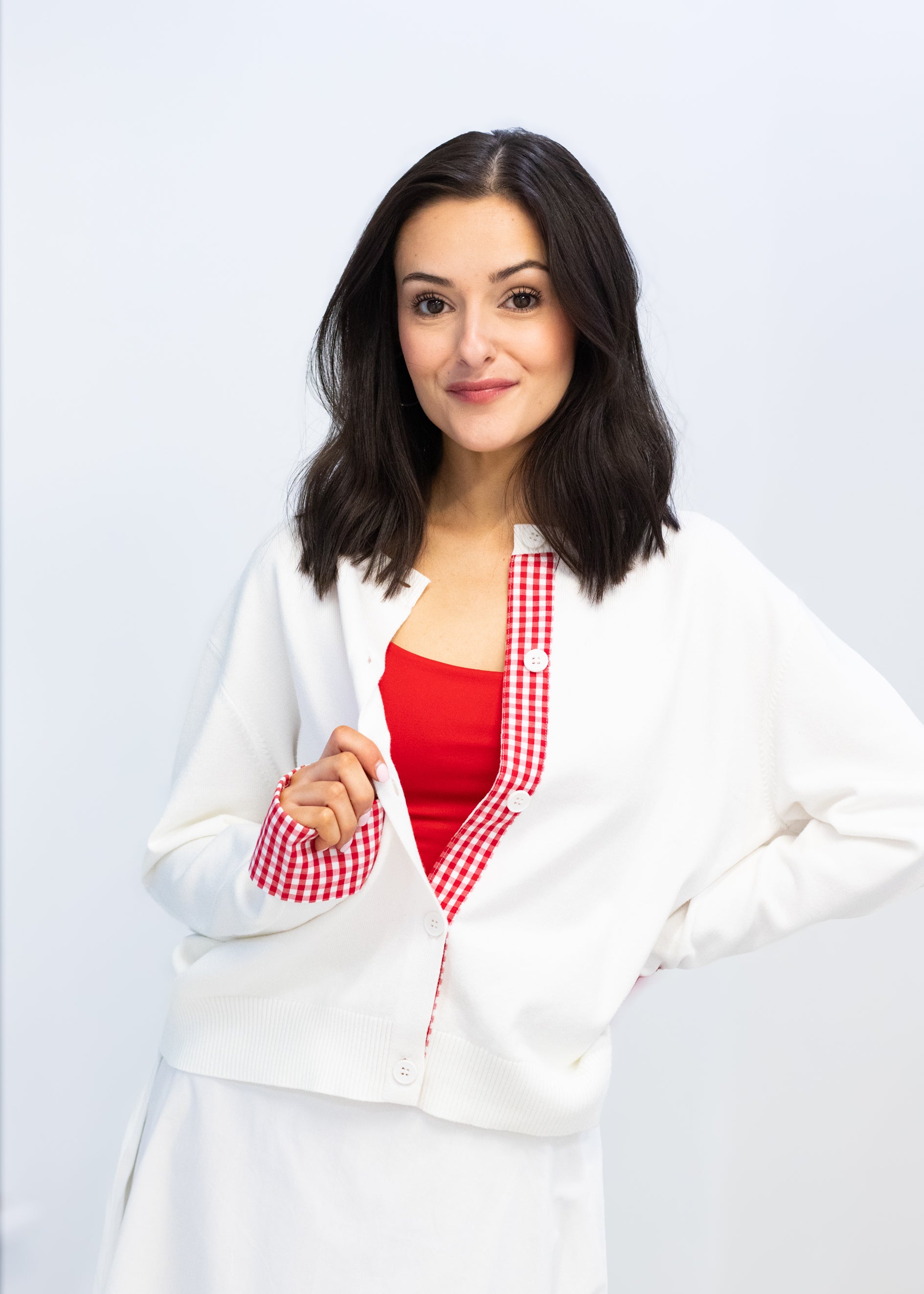 Woman wearing a white coat over a red shirt on a light gray background