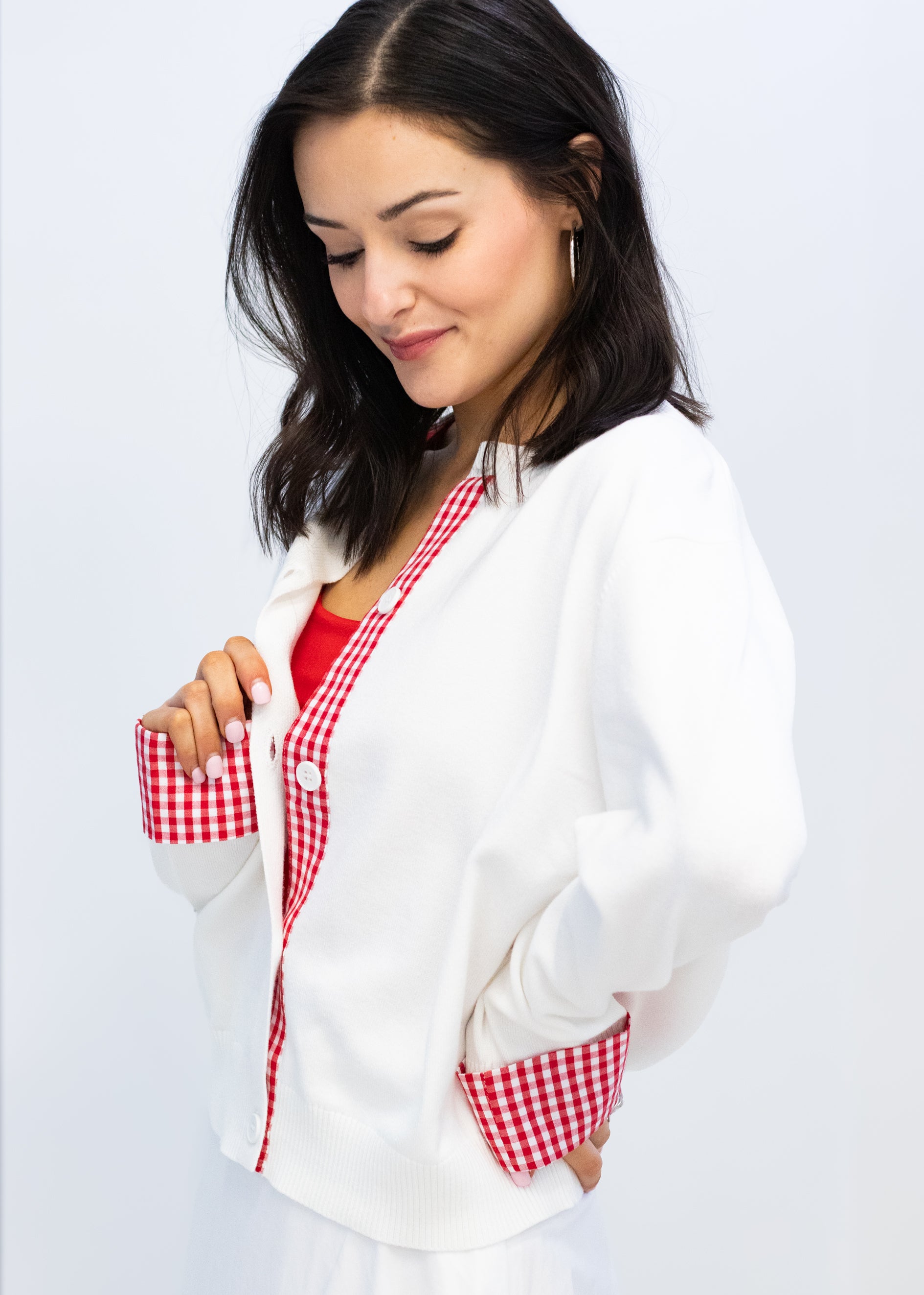 Woman wearing a white cardigan with red checkered pockets on a light gray background