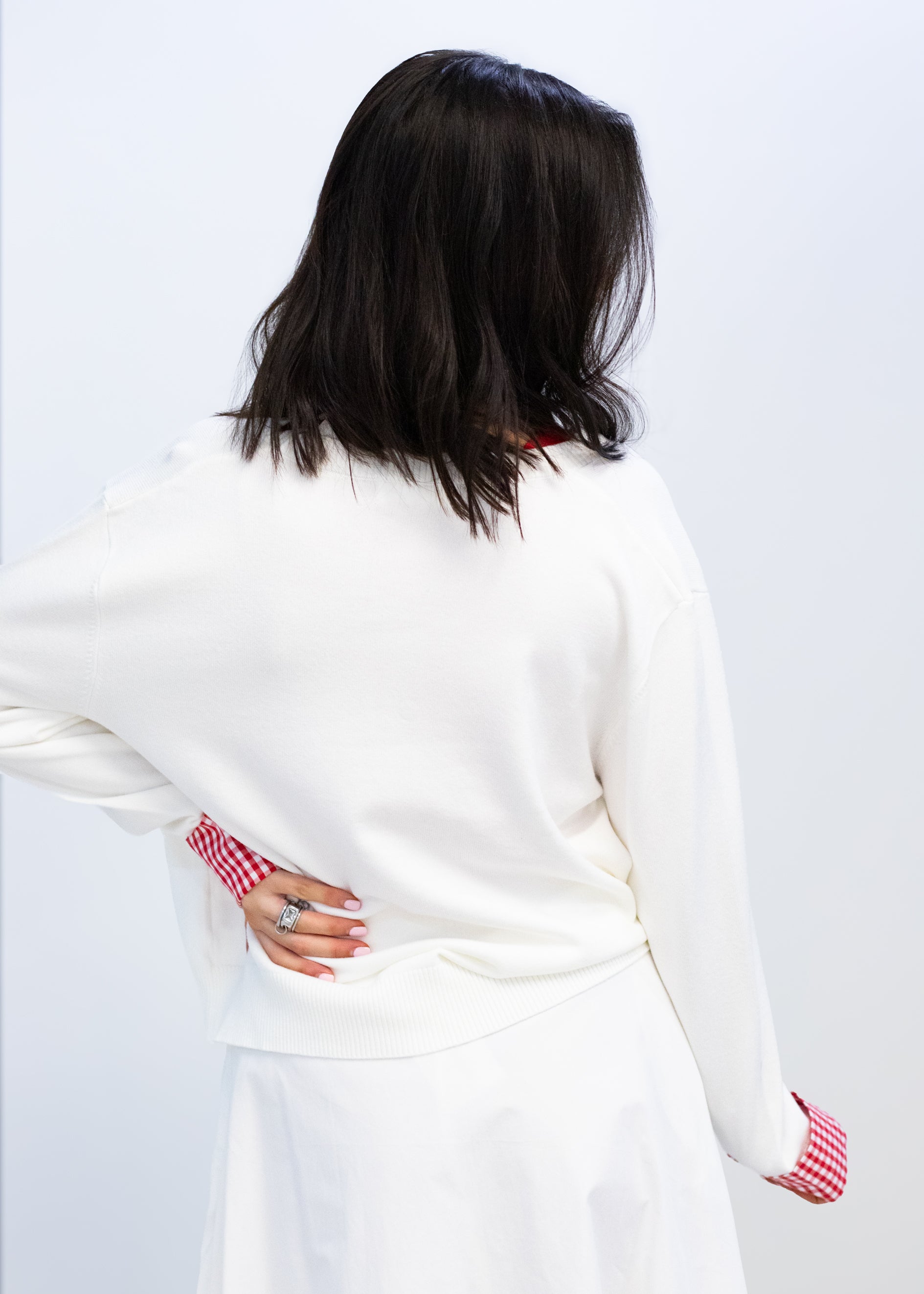 Person wearing a white sweater with red patterned cuffs on a plain background