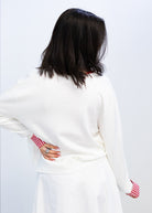 Person wearing a white sweater with red patterned cuffs on a plain background