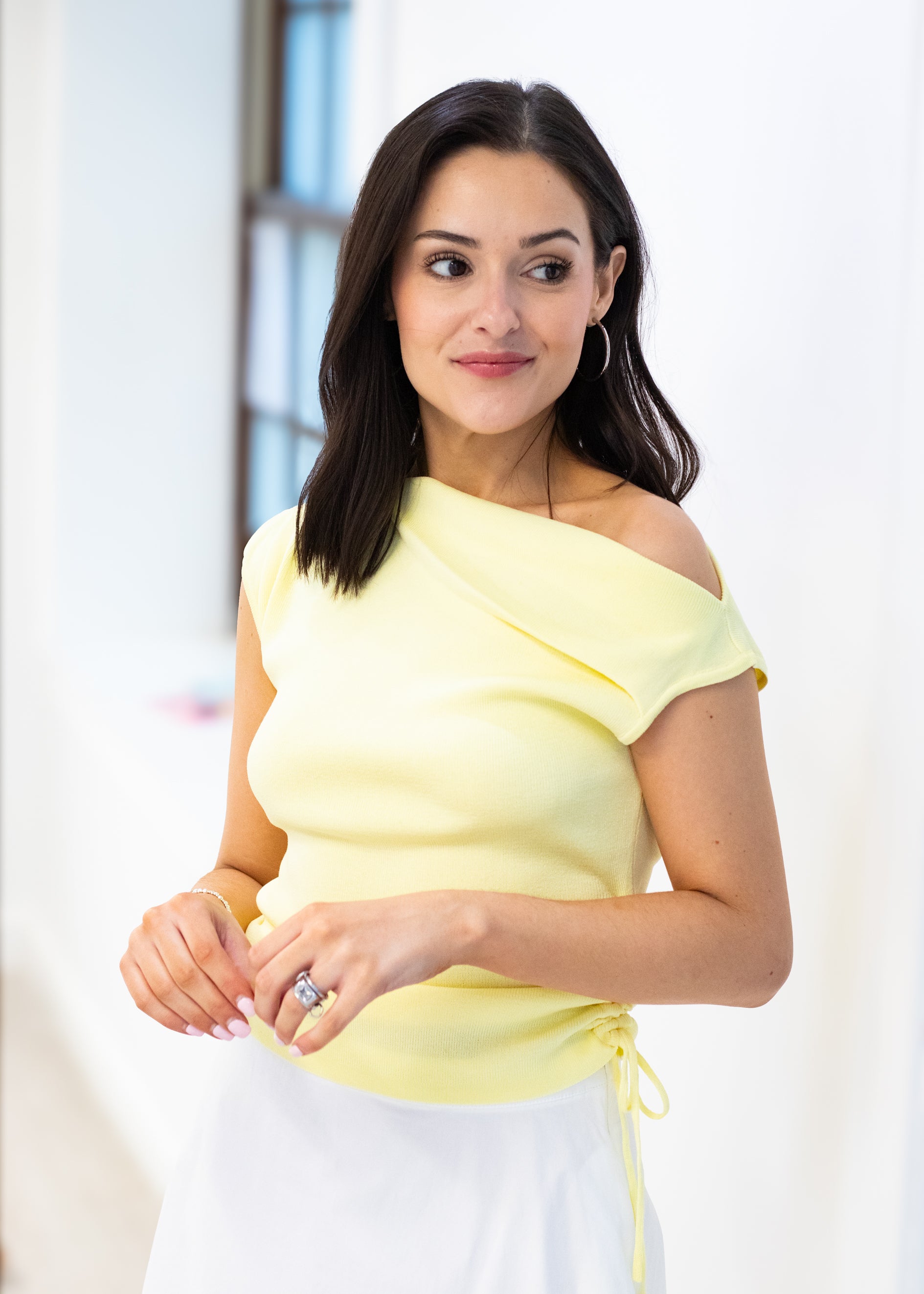 Woman wearing a yellow off-shoulder top with a blurred indoor background