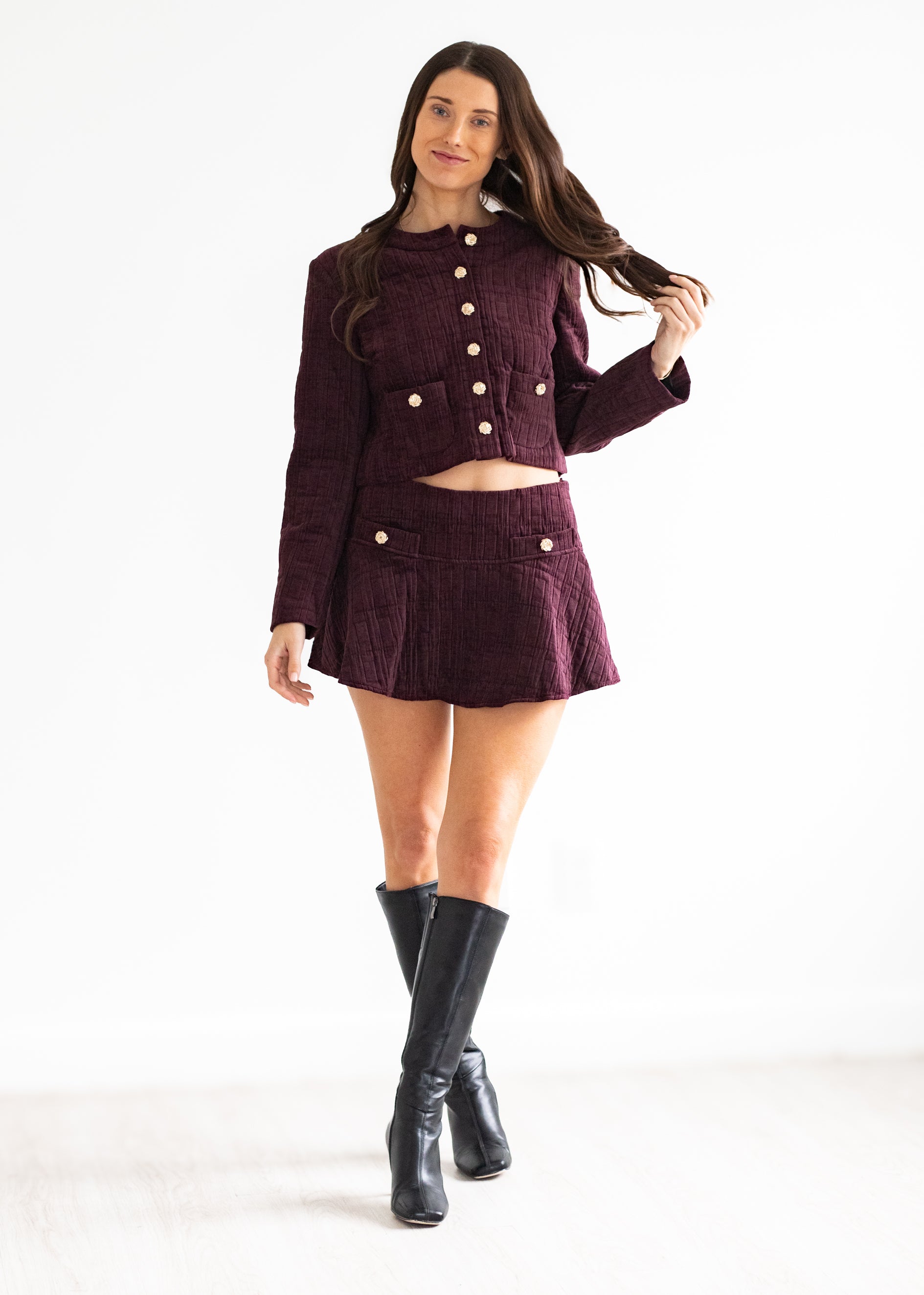 Woman wearing a maroon outfit with gold buttons on a white background