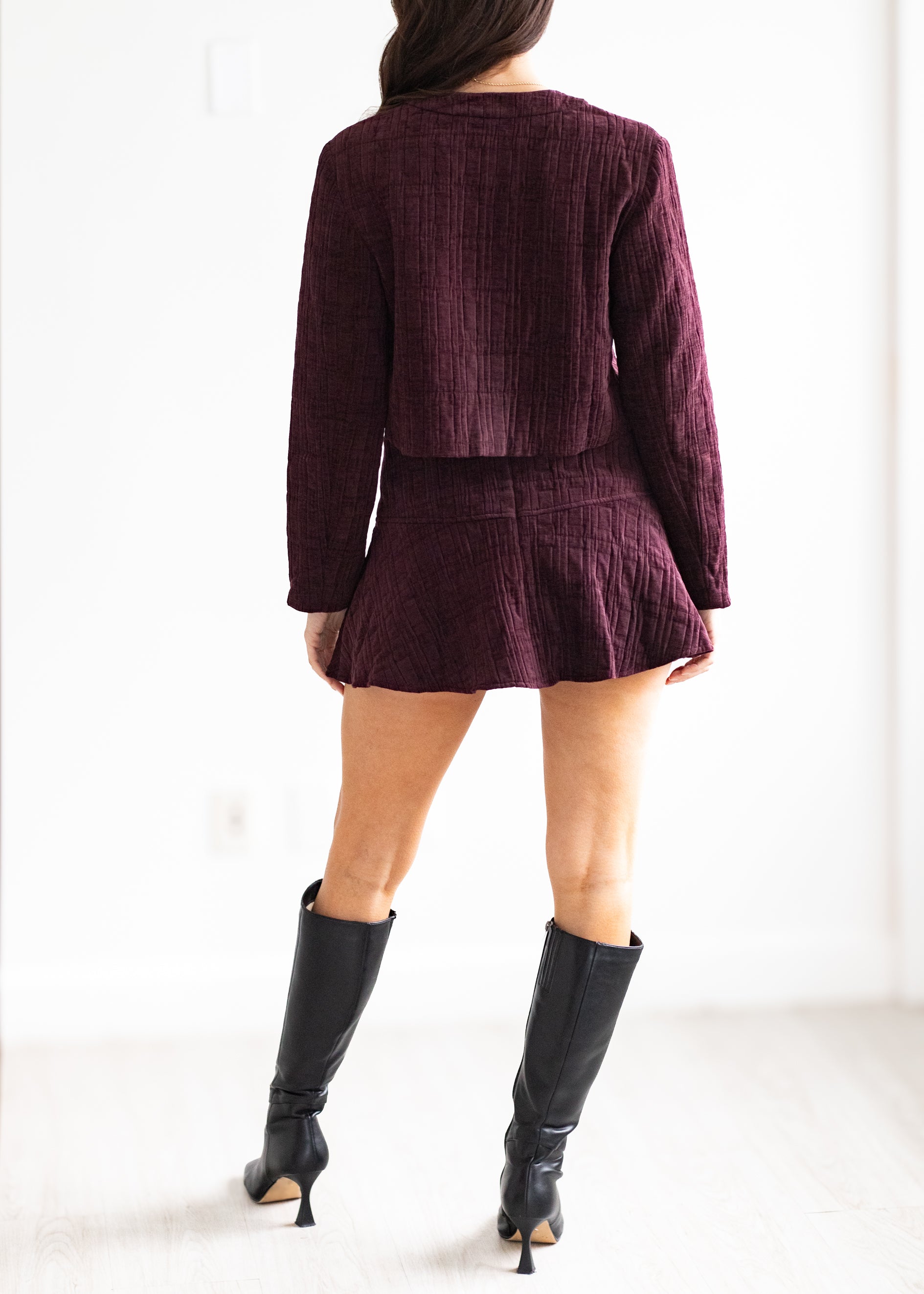 Person wearing a burgundy textured suit with black knee-high boots on a white background