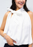 Woman wearing a white sleeveless top with a bow detail against a plain background