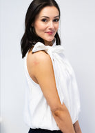 Woman wearing a white blouse with a bow detail on a plain background