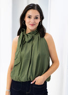 Woman wearing a green sleeveless top with a bow neckline against a white background