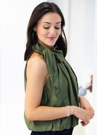 Woman wearing a green sleeveless top with a bow detail, standing against a white background.