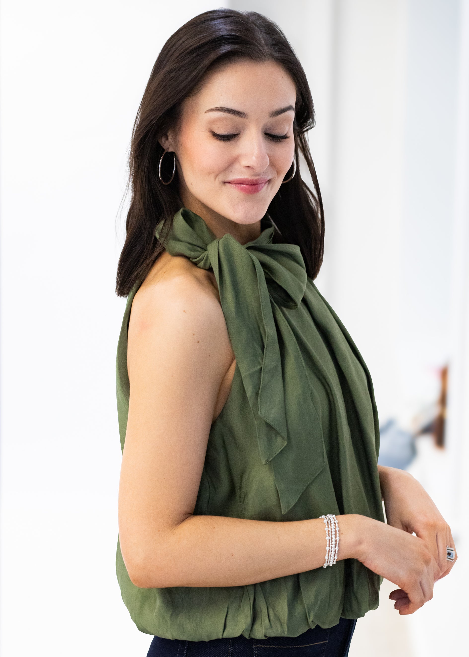 Woman wearing a green sleeveless top with a bow detail, standing against a white background.