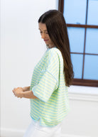 Woman wearing a light blue and yellow striped shirt in a room with a window.