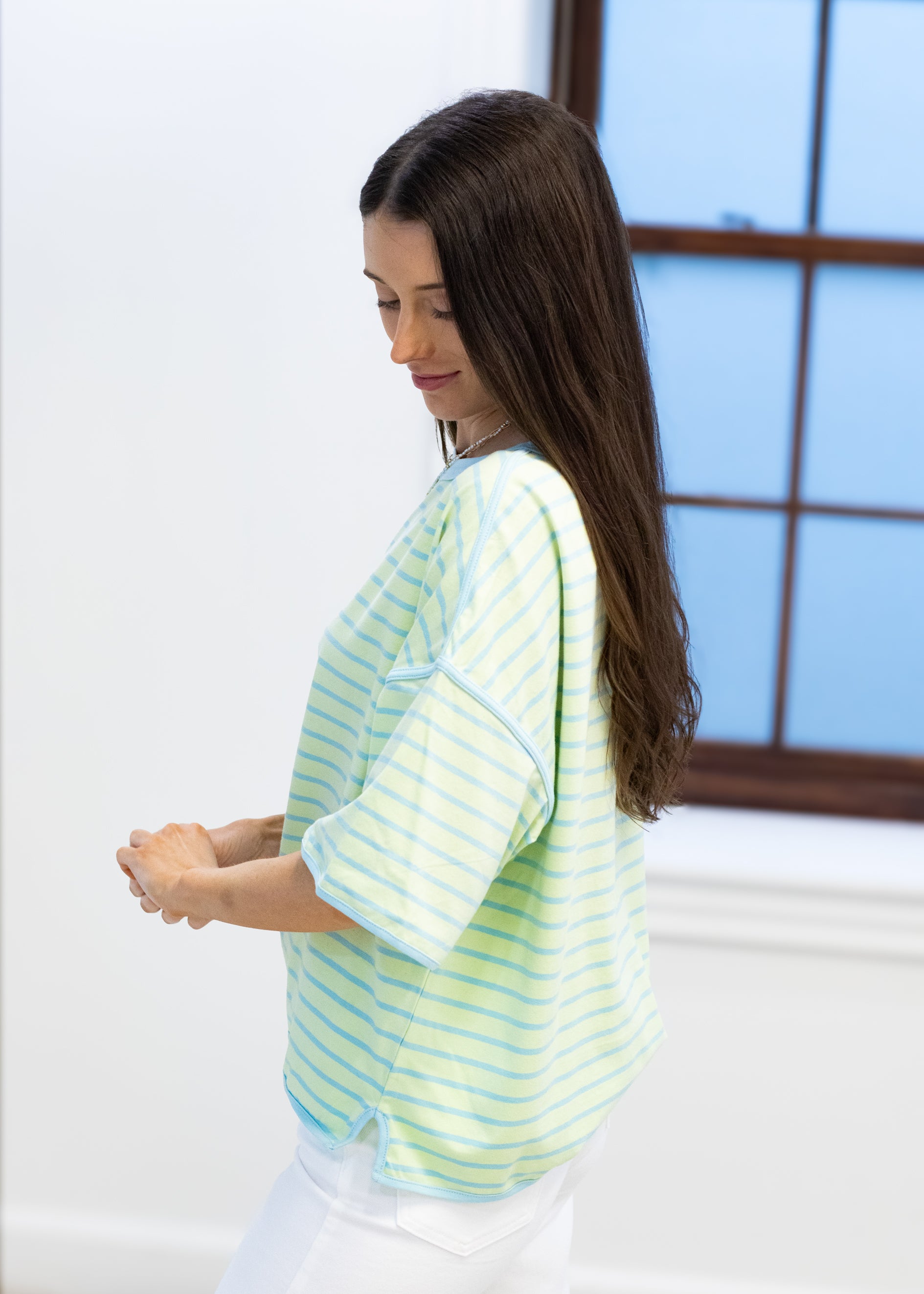 Woman wearing a light blue and yellow striped shirt in a room with a window.
