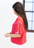 Woman wearing a red and white striped shirt sitting on a bed.
