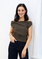 Woman wearing an off-shoulder brown top and dark jeans against a white background