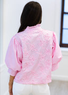 Person wearing a pink floral blouse with white pants against a light background