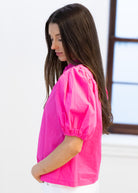 Woman wearing a bright pink blouse with a blurred background